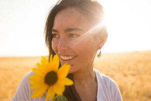 a woman wearing silver hawk hoop earrings and holding a sunflower in a field