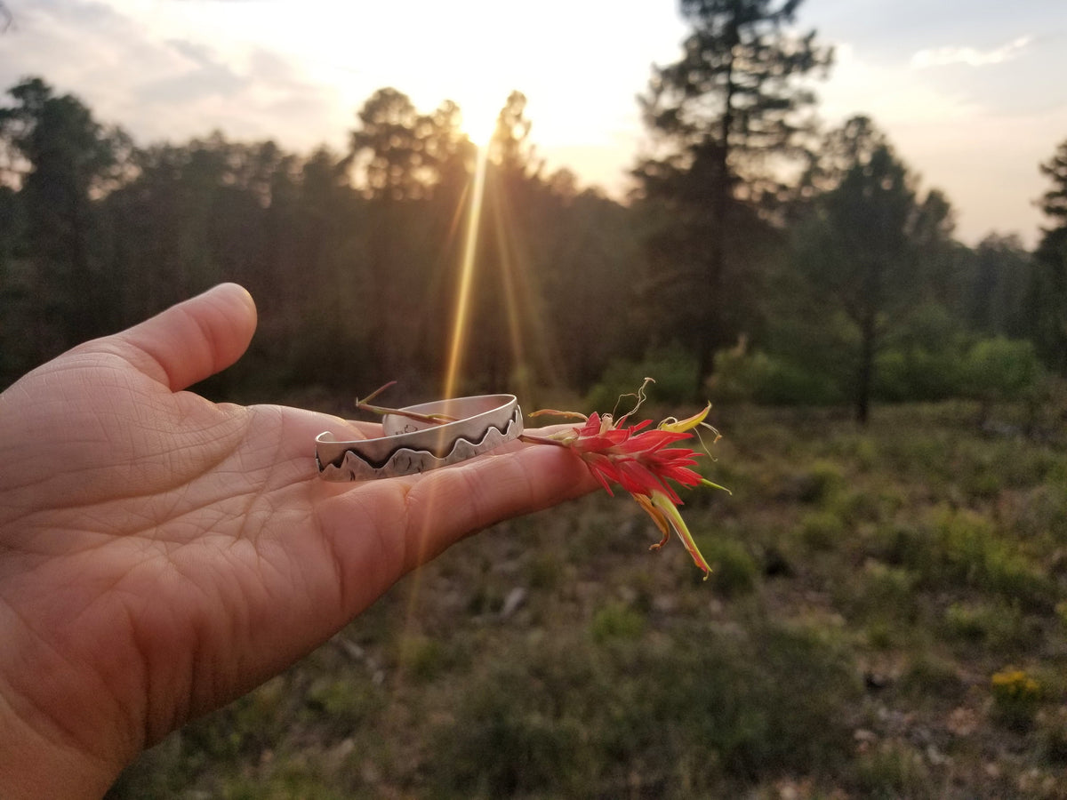 hand holding a silver mountain bracelet and indian paintbrush flower in a forested settings