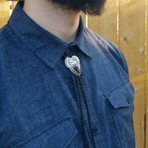 a man wearing a silver t-rex skull dinosaur bone bolo tie with leather cord