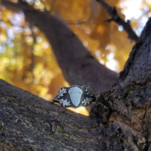 An acorn signet ring balanced on an oak branch with golden leaves in the background