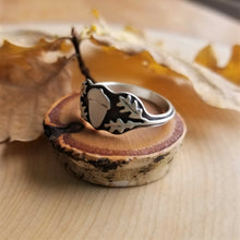 An acorn signet ring side view, sitting atop a tiny wood slice with golden oak leaves in the background