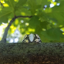 An acorn signet ring balanced on an oak branch with green leaves in the background