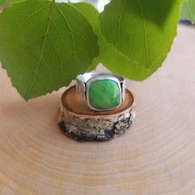 An aspen ring with a bright green stone sits atop a tiny wood slice, with green aspen leaves in the background