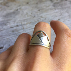 a hand wearing a silver mountain ring on the middle finger