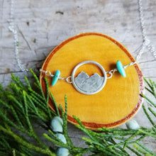 silver mountain necklace with turquoise beads resting on a wood slice with a juniper sprig