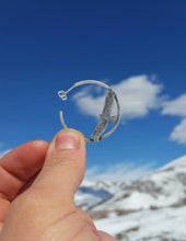 silver hawk hoop earring being held against snowy mountains and blue sky
