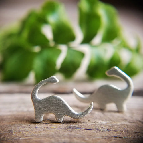 silver brontosaurus dinosaur stud earrings with a fern frond in the background